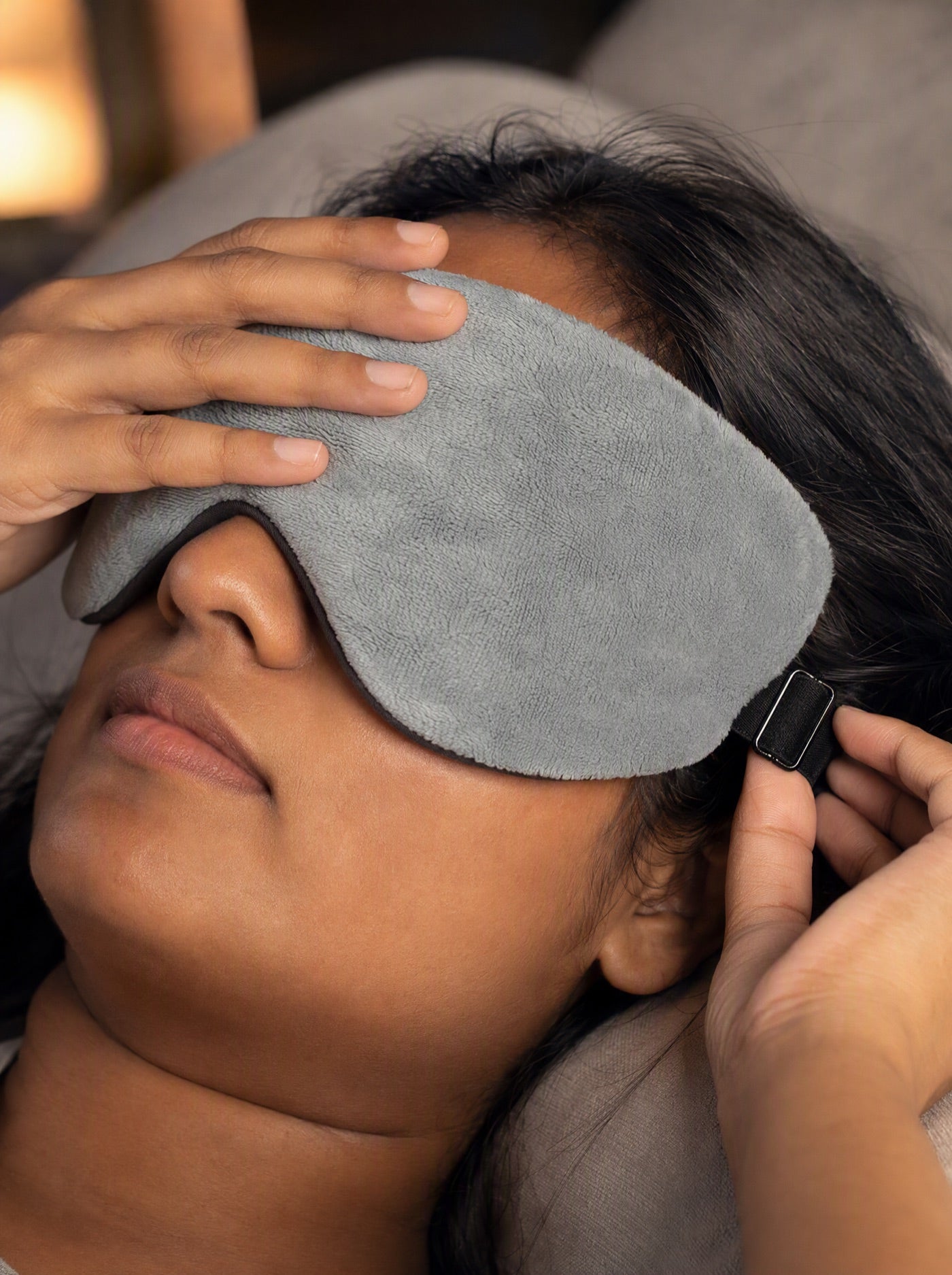 Person gently adjusting the black strap on the grey sleep mask