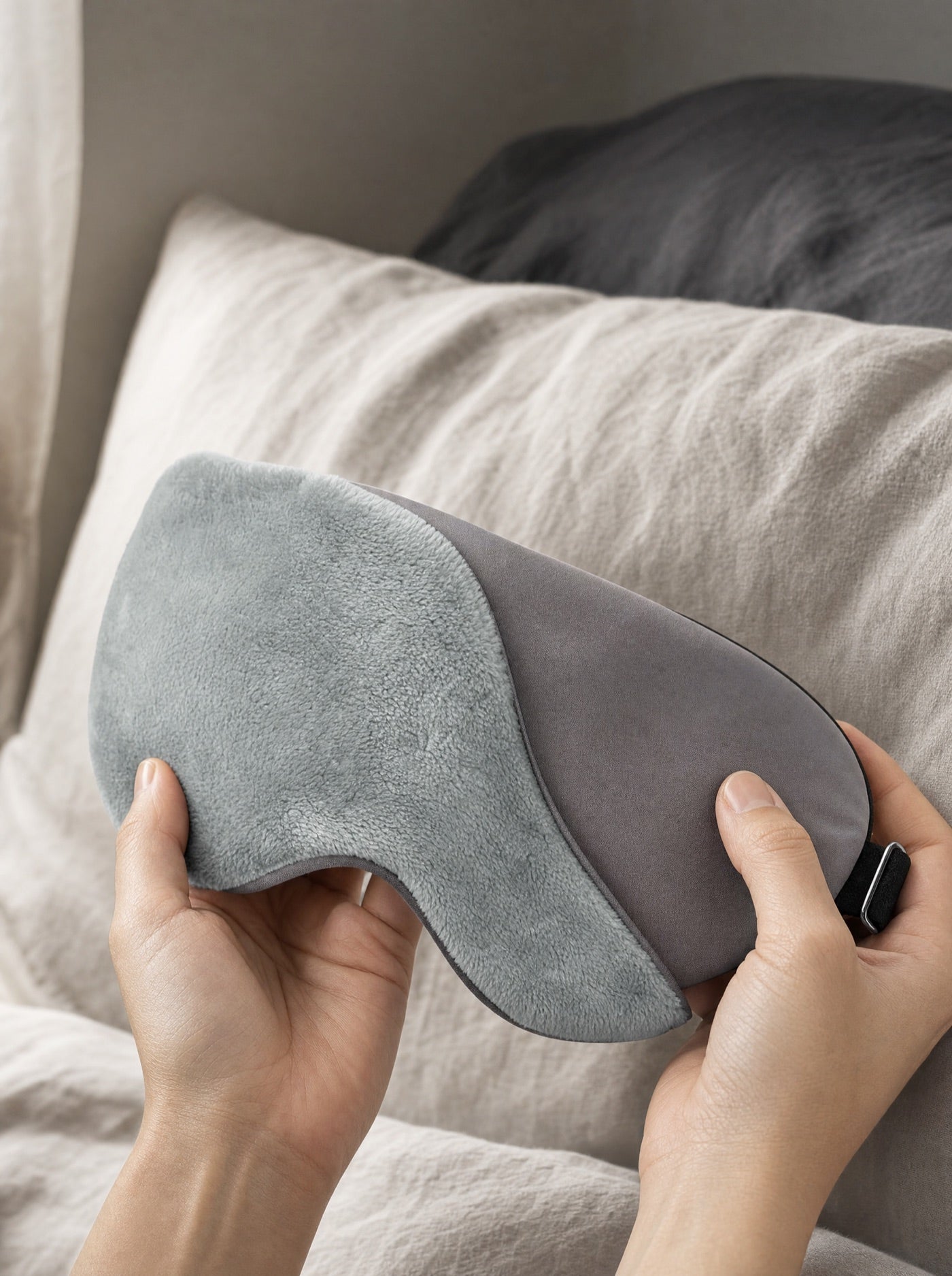 Hands showing the soft plush and smooth sides of the grey sleep mask